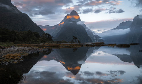 First sunrays lighting the peak of mountain with beautiful reflection in water, milford sound
