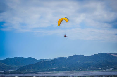 Person paragliding over sea against mountains