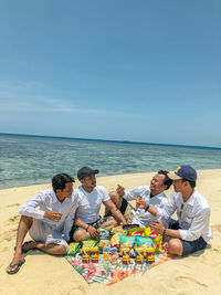 People sitting on beach by sea against sky