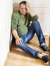 Depressed mature man sitting on hardwood floor at home