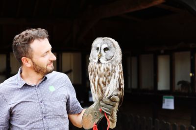 Handsome man with owl perching on hand
