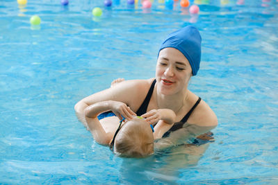 Toddler child learning to swim in indoor swimming pool with teacher. floating