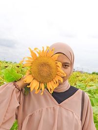 Young woman holding sunflower against sky