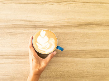 Cropped hand of woman holding coffee on table