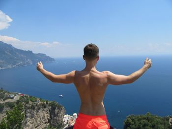 Rear view of shirtless man looking at sea against sky