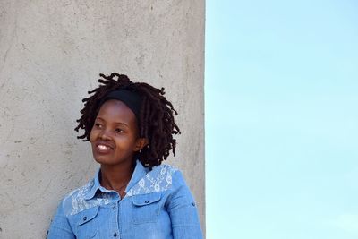 Thoughtful young woman looking away by wall against clear blue sky