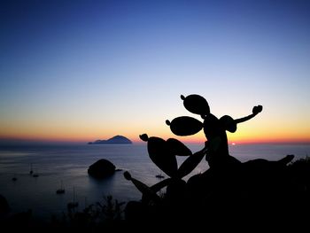 Silhouette men at beach against clear sky during sunset