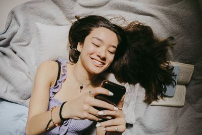 Directly above shot of smiling young woman using smart phone while lying on bed at home