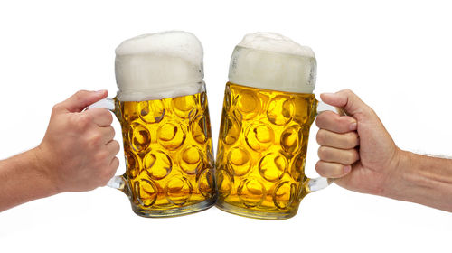 Close-up of hand holding beer glass against white background