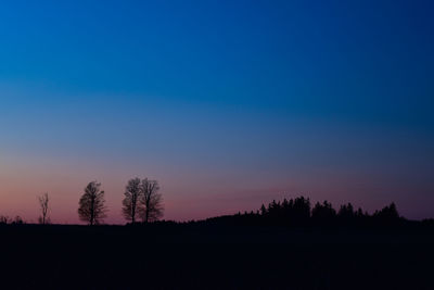 Silhouette trees on field against clear sky