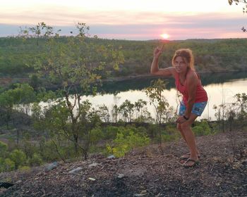 Full length of happy young woman standing on land against sky during sunset