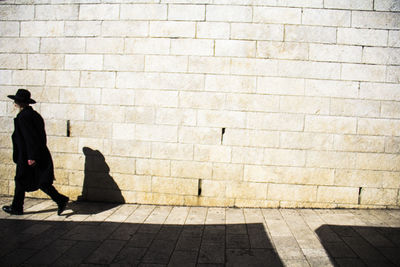 Rear view of woman walking on footpath against wall