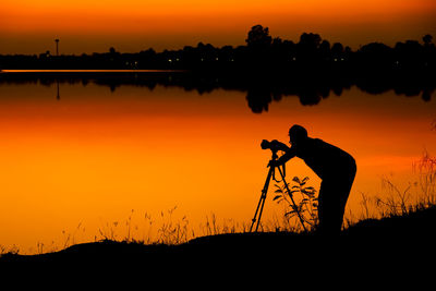 Silhouette man photographing against sky during sunset