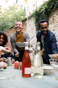 Smiling man and woman serving food to friends at dining table during party in back yard