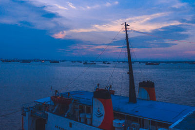 Sailboats moored in sea against sky during sunset