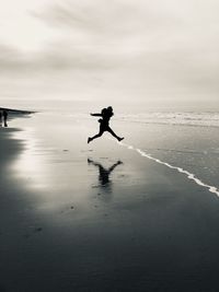 Full length of excited silhouette woman jumping on shore at beach against sky