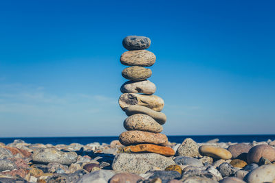 Stack of stones at sea shore against blue sky