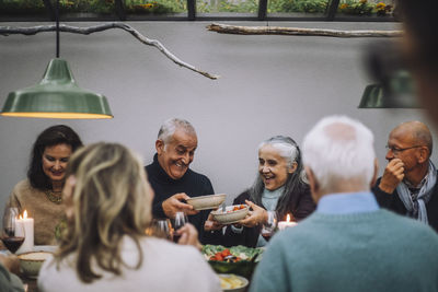 Happy male and female friends passing food bowls during dinner party