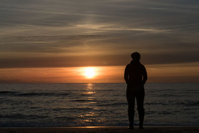 Full length of man standing on beach against sky during sunrise