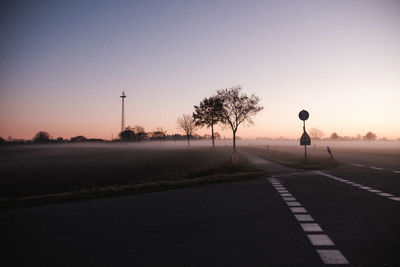 Road by silhouette trees against clear sky at sunset