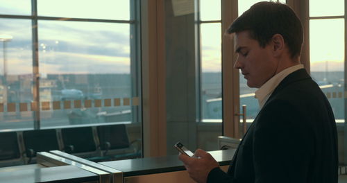 Side view of young man using mobile phone at window