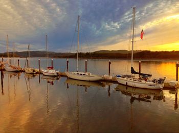 Boats in lake against cloudy sky at sunset