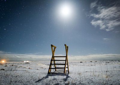 Wooden ladder on snow covered landscape against sky