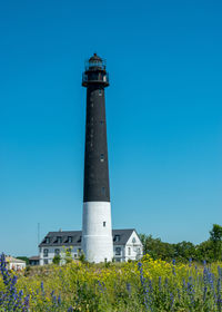 Lighthouse by sea against clear blue sky