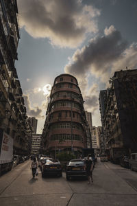 Cars on city street by buildings against sky