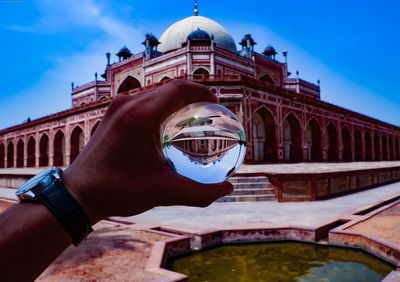 Cropped image of hand holding historical building against sky
