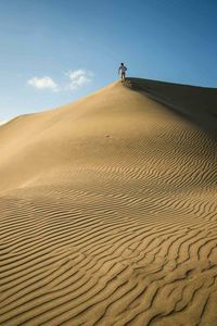 Man walking on sand dune in desert against sky