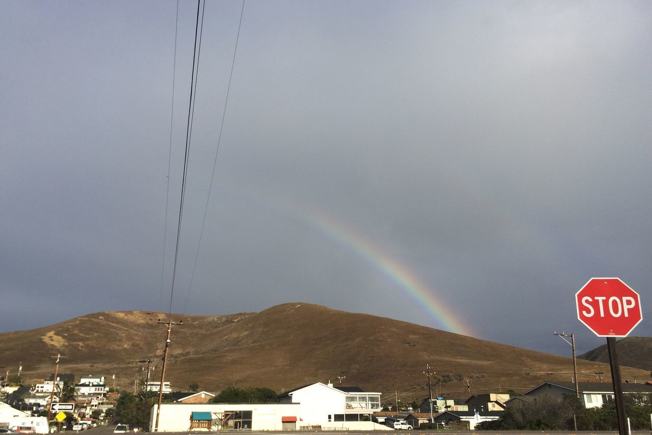 rainbow, multi colored, building exterior, built structure, mountain, architecture, scenics, beauty in nature, sky, natural phenomenon, nature, mountain range, tranquil scene, day, town, outdoors, tranquility, power supply, majestic, no people, residential district