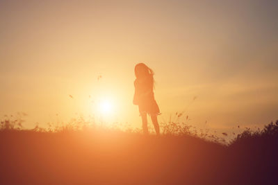 Rear view of silhouette woman standing against sky during sunset