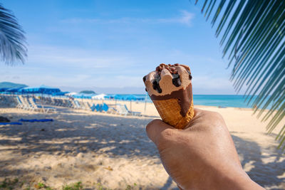 Cropped hand holding ice cream cone against sea