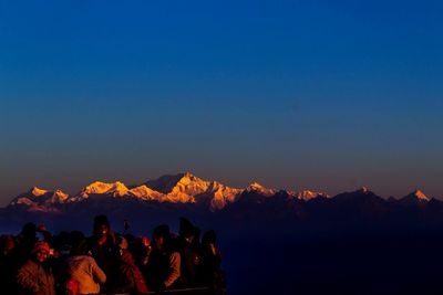 People standing against mountains and sky at sunset