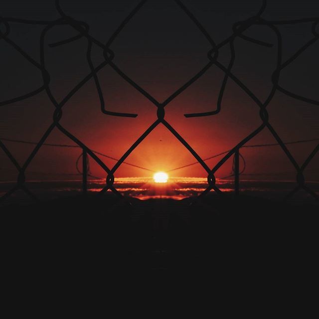 sunset, sun, silhouette, orange color, protection, fence, safety, scenics, tranquility, sky, sunlight, nature, beauty in nature, security, tranquil scene, idyllic, clear sky, chainlink fence, outdoors, no people