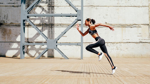 Side view of young woman running on walkway during sunny day