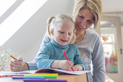 Mother assisting daughter in coloring book at home