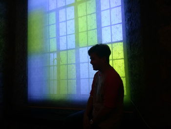 Side view of silhouette man standing against illuminated window