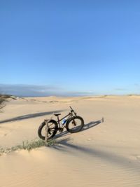 Bicycle on sand against clear sky