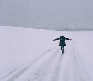 Full length rear view of woman walking on snowy field during snowfall