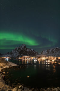 Illuminated city by mountains against sky at night