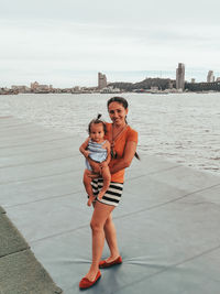 Portrait of happy girl with baby girl standing against sea