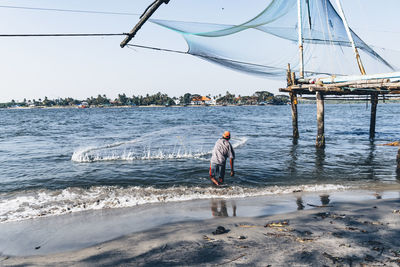 Rear view of man fishing in sea against sky