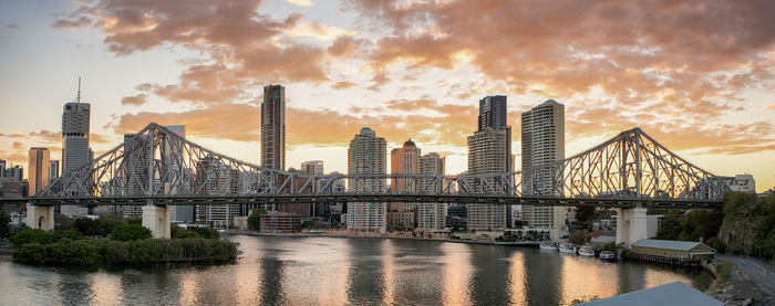 Bridge over river in city against cloudy sky