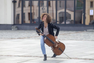 Smiling woman holding violin while dancing on street