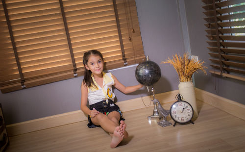 Full length portrait of cute smiling girl sitting on floor at home