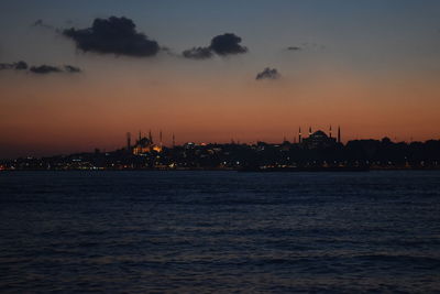 Silhouette buildings by sea against sky during sunset