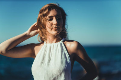 Close-up of young woman standing at beach against clear blue sky