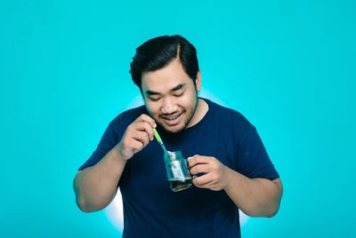 Young man drinking glass against blue background